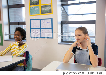 Diverse teenage female students smiling, studying at classroom desks with notebooks, laptop Diverse teenage female students smiling, studying at classroom desks with notebooks, laptop 140561308