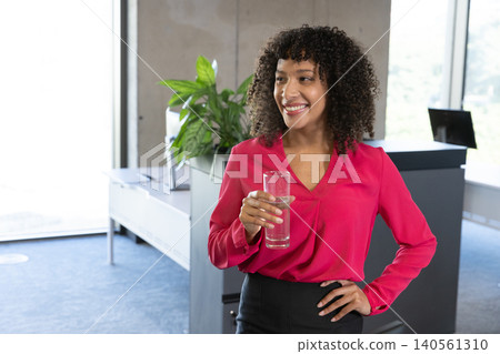 African american woman in business attire standing in office reception with tall glass of water African american woman in business attire standing in office reception with tall glass of water 140561310