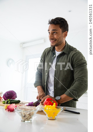 Man chopping vegetables at kitchen island on cutting board with chef's knife Man chopping vegetables at kitchen island on cutting board with chef's knife 140561331