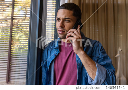 Man talking on smartphone by sliding glass door at home with blinds and curtains Man talking on smartphone by sliding glass door at home with blinds and curtains 140561341
