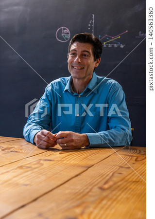 Male lecturer presenting in classroom with table and chalkboard with pie and line graphs Male lecturer presenting in classroom with table and chalkboard with pie and line graphs 140561360