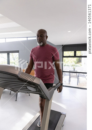 Senior african american man walking on treadmill in home gym wearing t-shirt and smartwatch Senior african american man walking on treadmill in home gym wearing t-shirt and smartwatch 140561371
