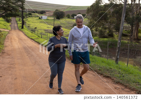 Diverse couple walking side by side along gravel farm track beside wire fence, utility poles Diverse couple walking side by side along gravel farm track beside wire fence, utility poles 140561372