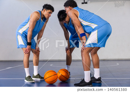 African american male teen basketball players huddling on gym court with orange basketballs African american male teen basketball players huddling on gym court with orange basketballs 140561380