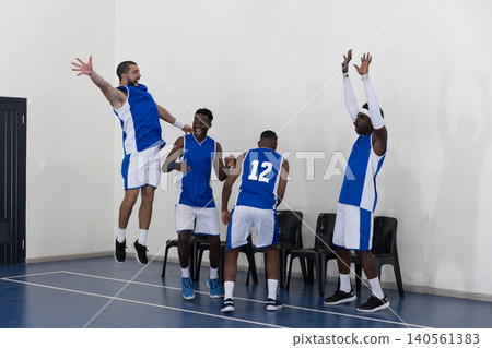 Diverse male basketball teammates celebrating on sideline at gym court wearing uniforms Diverse male basketball teammates celebrating on sideline at gym court wearing uniforms 140561383