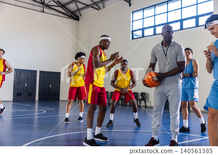 African american coach holding basketball with whistle leading red-yellow, blue teams on court African american coach holding basketball with whistle leading red-yellow, blue teams on court 140561385