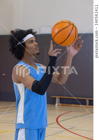 African american male spinning basketball on fingertip in gym headband black sleeve by bench African american male spinning basketball on fingertip in gym headband black sleeve by bench 140561411