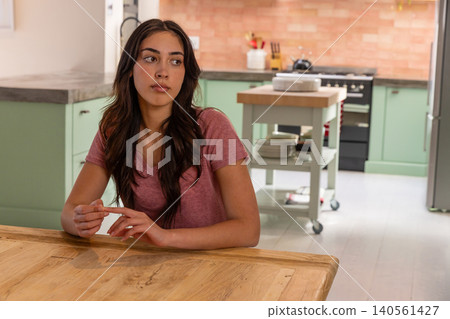 Woman sitting at kitchen table, wearing maroon t-shirt next to rolling island and stove Woman sitting at kitchen table, wearing maroon t-shirt next to rolling island and stove 140561427