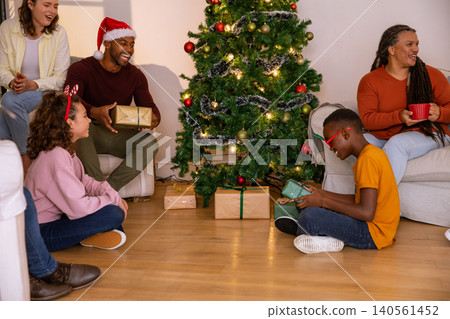 Diverse family unwrapping gifts, christmas tree with string lights in living room 140561452