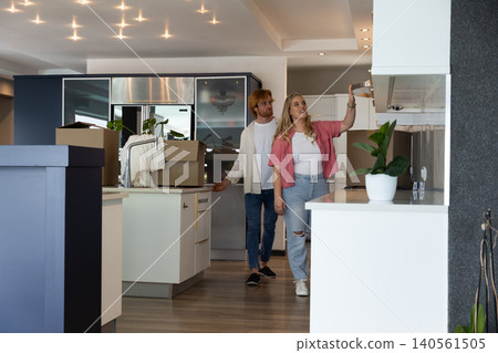 Couple inspecting kitchen cabinetry and gesturing toward moving boxes on island Couple inspecting kitchen cabinetry and gesturing toward moving boxes on island 140561505