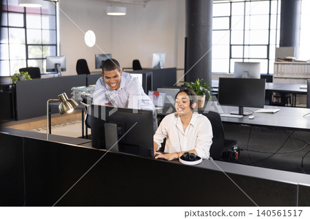 Diverse coworkers in business attire typing on keyboard and leaning over monitor at office Diverse coworkers in business attire typing on keyboard and leaning over monitor at office 140561517