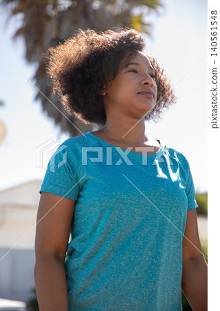 Mid adult african american woman standing by palm tree on sunny street corner and gazing Mid adult african american woman standing by palm tree on sunny street corner and gazing 140561548