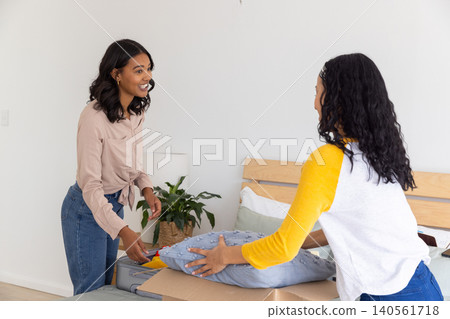 Diverse mom and teenage daughter placing blue patterned cushion on bed with white linens in bedroom Diverse mom and teenage daughter placing blue patterned cushion on bed with white linens in bedroom 140561718