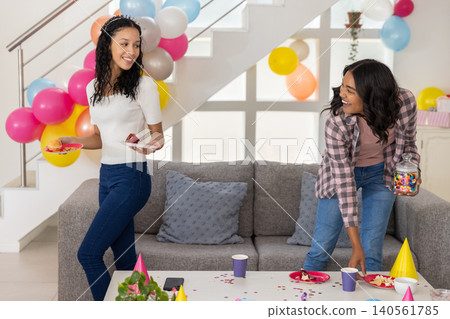 Diverse mom and teenage daughter preparing candy treats on coffee table in room 140561785