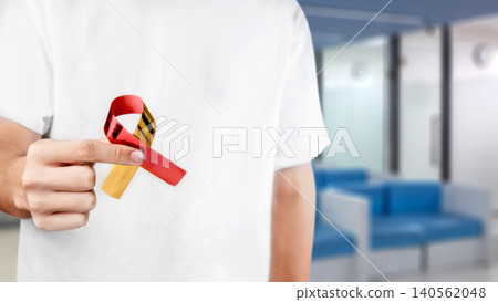 Close-up of a person holding a red and yellow ribbon for Hepatitis awareness in a clinic Close-up of a person holding a red and yellow ribbon for Hepatitis awareness in a clinic 140562048