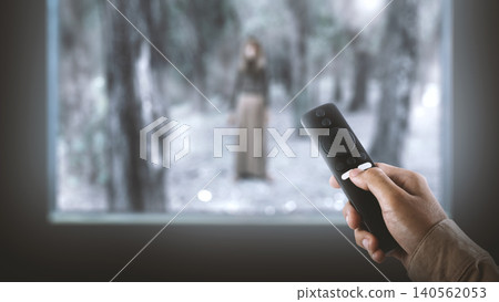 Close-up of a hand using a remote control to stream a spooky horror movie featuring a ghostly figure on screen Close-up of a hand using a remote control to stream a spooky horror movie featuring a ghostly figure on screen 140562053