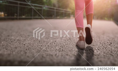 A close-up, low-angle shot of a woman walking on an outdoor path, wearing pink leggings and white sneakers, capturing a sense of active lifestyle and motion A close-up, low-angle shot of a woman walking on an outdoor path, wearing pink leggings and white sneakers, capturing a sense of active lifestyle and motion 140562054