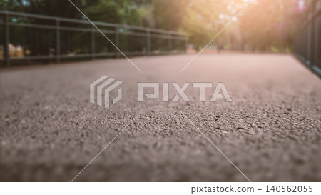 A close-up, low-angle perspective of an asphalt walkway winding through a park, with railings on both sides and soft sunlight filtering through the trees in the background A close-up, low-angle perspective of an asphalt walkway winding through a park, with railings on both sides and soft sunlight filtering through the trees in the background 140562055