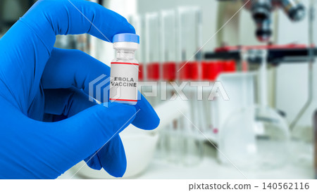 A close-up view of a medical professional wearing blue latex gloves holding a small vial labeled Ebola Vaccine, with laboratory glassware and research equipment in the blurred background A close-up view of a medical professional wearing blue latex gloves holding a small vial labeled Ebola Vaccine, with laboratory glassware and research equipment in the blurred background 140562116