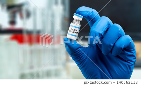 A researcher wearing a blue nitrile glove holds a small glass vial labeled Ebola Vaccine in a laboratory environment A researcher wearing a blue nitrile glove holds a small glass vial labeled Ebola Vaccine in a laboratory environment 140562118
