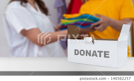 White donation box on a table with volunteers sorting and giving colorful clothes in the blurred background White donation box on a table with volunteers sorting and giving colorful clothes in the blurred background 140562257