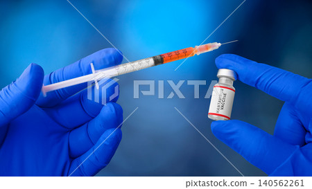 A medical professional in blue gloves holds a syringe filled with orange liquid next to a Hantavirus vaccine vial A medical professional in blue gloves holds a syringe filled with orange liquid next to a Hantavirus vaccine vial 140562261