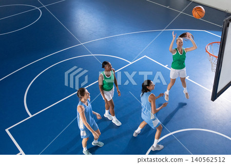 Diverse female players shooting and guarding basketball hoop on court in jerseys, copy space Diverse female players shooting and guarding basketball hoop on court in jerseys, copy space 140562512