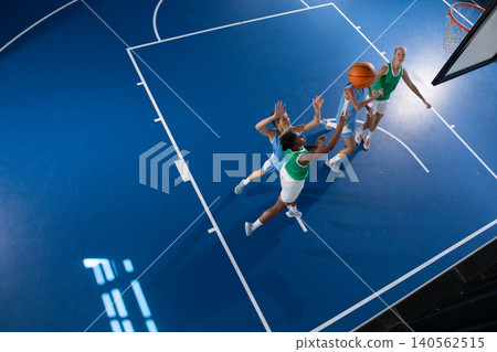 Female basketball players in uniform jumping and contesting layup in gym by hoop, copy space Female basketball players in uniform jumping and contesting layup in gym by hoop, copy space 140562515