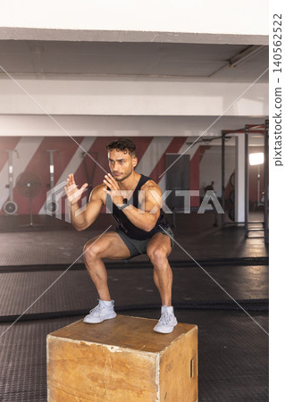 Man balancing on wooden plyometric box on rubber flooring in functional gym with battle ropes 140562522