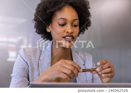 African american businesswoman wearing blazer holding usb drive, examining laptop at office desk African american businesswoman wearing blazer holding usb drive, examining laptop at office desk 140562526
