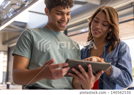 Diverse coworkers collaborating on touchscreen tablet in office space with exposed ductwork Diverse coworkers collaborating on touchscreen tablet in office space with exposed ductwork 140562530