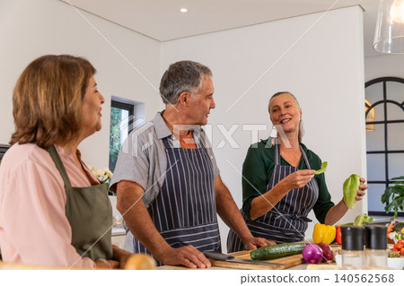 Senior friends slicing cucumber on cutting board at modern kitchen island, using spice grinders 140562568
