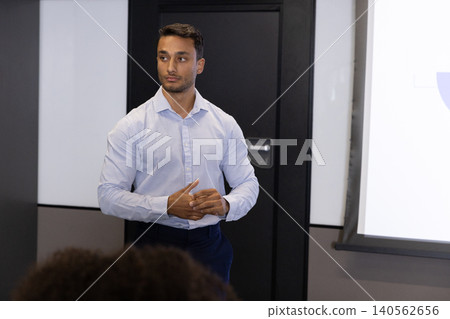 Asian man delivering presentation in meeting room with projection screen in business attire Asian man delivering presentation in meeting room with projection screen in business attire 140562656