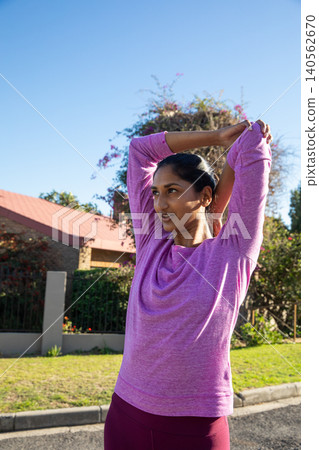 Asian indian woman stretching arms overhead on street in front of brick house 140562670