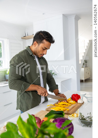 Asian man slicing bell pepper with chef's knife on wooden cutting board at kitchen island Asian man slicing bell pepper with chef's knife on wooden cutting board at kitchen island 140562674