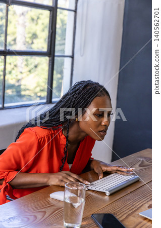 African american woman leaning in, focusing on computer at office desk with keyboard, smartphone African american woman leaning in, focusing on computer at office desk with keyboard, smartphone 140562701