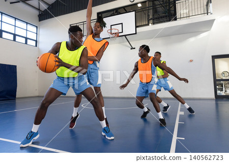 African american male athlete wearing yellow bib pivoting and protecting basketball on court African american male athlete wearing yellow bib pivoting and protecting basketball on court 140562723
