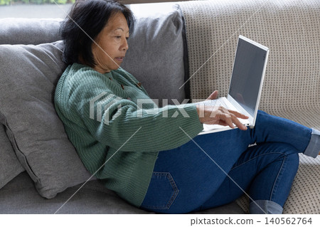 Senior asian woman sitting on couch working on white laptop in living room, copy space Senior asian woman sitting on couch working on white laptop in living room, copy space 140562764
