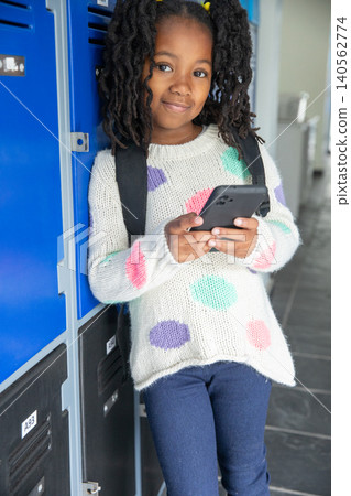 African american girl using phone with backpack in hall next to metal lockers and fountain African american girl using phone with backpack in hall next to metal lockers and fountain 140562774