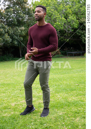 African american man standing on grassy lawn wearing burgundy knit sweater and jogger pants African american man standing on grassy lawn wearing burgundy knit sweater and jogger pants 140562785