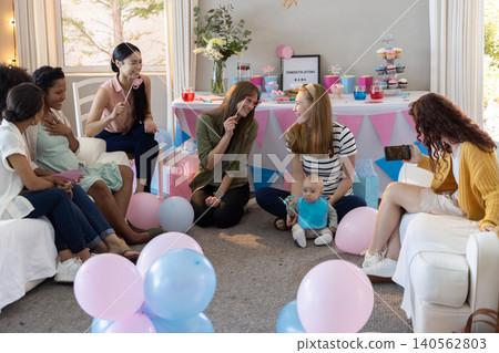 Female friends celebrating baby shower in living room congratulations mama sign cupcakes Female friends celebrating baby shower in living room congratulations mama sign cupcakes 140562803