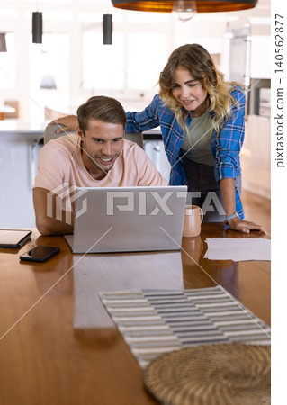 Couple working together at wooden table in kitchen using laptop smartphone notebook coffee mug Couple working together at wooden table in kitchen using laptop smartphone notebook coffee mug 140562877