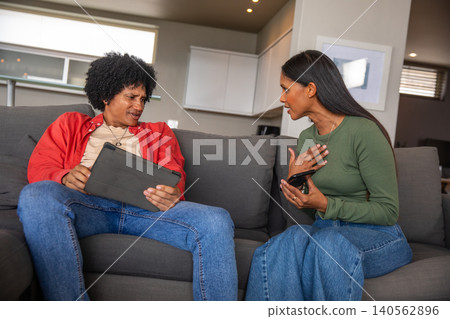 African american and asian indian couple sitting on sofa in living room with tablet, smartphone African american and asian indian couple sitting on sofa in living room with tablet, smartphone 140562896