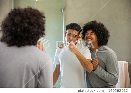 Diverse male friends brushing their teeth at modern bathroom sink with toothbrushes and towel rack Diverse male friends brushing their teeth at modern bathroom sink with toothbrushes and towel rack 140562912