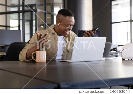 African american man checking smartphone in modern office, using laptop, vr headset African american man checking smartphone in modern office, using laptop, vr headset 140563044