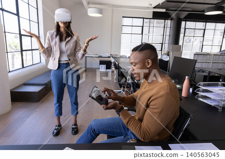 Diverse coworkers tapping tablet and wearing vr headset at open-plan office Diverse coworkers tapping tablet and wearing vr headset at open-plan office 140563045