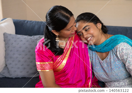 Indian mother and daughter wearing saree and kurta, sharing moment while sitting on dark blue sofa Indian mother and daughter wearing saree and kurta, sharing moment while sitting on dark blue sofa 140563122