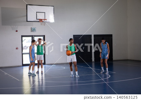 Diverse female athletes facing off on polished gymnasium court under hoop with basketball Diverse female athletes facing off on polished gymnasium court under hoop with basketball 140563125