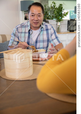 Asian family sharing noodles at dining table at home with bamboo steamers Asian family sharing noodles at dining table at home with bamboo steamers 140563160