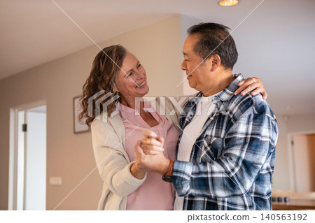 Diverse senior couple dancing in living room under recessed lights with picture Diverse senior couple dancing in living room under recessed lights with picture 140563192